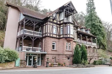 Ein historisches Gebäude mit einem charmanten, traditionellen Fassadenstil. Die Umgebung ist von Bäumen und Pflanzen umgeben, was eine einladende Atmosphäre schafft.