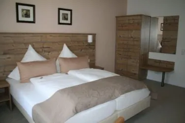 Ein gemütliches Schlafzimmer mit einem großen Bett und modernem Holzdekor. Die Wände sind in sanften Farben gehalten und es gibt einen Spiegel sowie Bilder an der Wand.