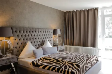 Ein modernes Schlafzimmer mit einem eleganten, gepolsterten Bett und einem gestreiften Zebradecken. Die Gardinen sind dunkelgrau und schaffen eine gemütliche Atmosphäre.