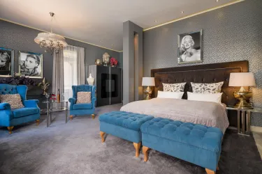 Ein stilvolles Schlafzimmer mit einem großen Bett und blauen Polstern. An den Wänden hängen Bilder von berühmten Persönlichkeiten.