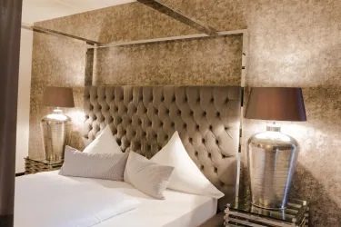 Ein elegantes Hotelzimmer mit einem gepolsterten Kopfteil und modernen Nachttischen. Die Beleuchtung ist sanft und schafft eine gemütliche Atmosphäre.