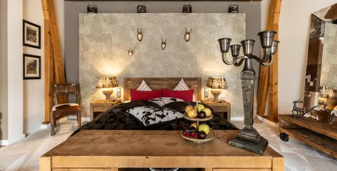 Ein stilvolles Schlafzimmer mit einem großen Bett und rustikalen Holzmöbeln. Die Wände sind dekoriert und eine elegante Kerze steht auf dem Tisch.