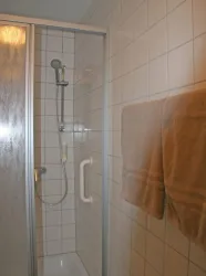 Eine Dusche mit Fliesenwänden und einem Handtuch an der Wand. Der Duschbereich ist klar und gut beleuchtet.