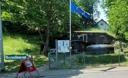 Ein ehemaliges Bunkergebäude mit einem EU-Flagge im Vordergrund. Daneben befindet sich ein Schild für das Westwallmuseum.