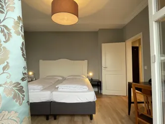Ein gemütliches Schlafzimmer mit zwei Einzelbetten und einem großen Fenster. Die Wände sind in sanften Farben gehalten, und eine Lampe sorgt für angenehmes Licht.