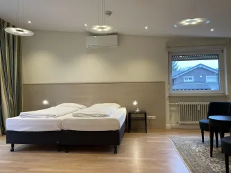 Ein modernes Zimmer mit zwei Einzelbetten und Holzfußboden. Es gibt einen kleinen Tisch und Stühle sowie ein großes Fenster mit Blick nach draußen.