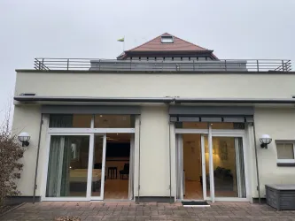 Ein modernes Gebäude mit großen Fenstern und einer Terrasse. Der Himmel ist bewölkt und es sieht nach einem ruhigen Tag aus.