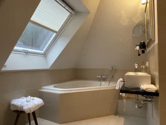 Ein modernes Badezimmer mit einer Badewanne und einem großen Fenster. Es gibt einen kleinen Tisch mit Handtüchern und Spiegel.