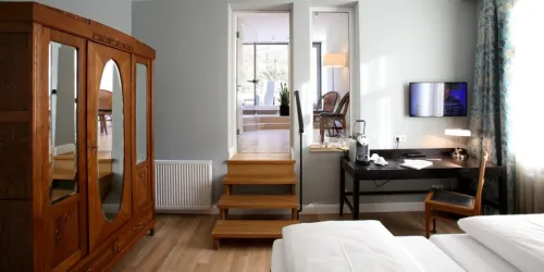 Ein modernes Schlafzimmer mit einem großen Holzschrank und einem Schreibtisch. Treppen führen zu einem hellen Wohnbereich im Hintergrund.