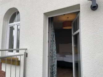 Ein offenes Fenster mit Aussicht auf ein helles Schlafzimmer. Der Raum wirkt gemütlich und einladend.