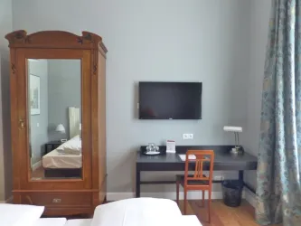 Ein gemütliches Schlafzimmer mit einem großen Holzschrank und einem modernen Fernseher an der Wand. Ein Schreibtisch mit einer Lampe und einem Stuhl ergänzt die Einrichtung.