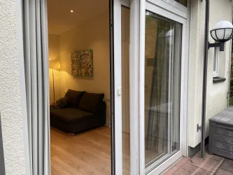 Ein gemütlicher Wohnraum mit einem Sofa und einer Stehlampe. Die Glastür öffnet sich zu einem kleinen Balkon.