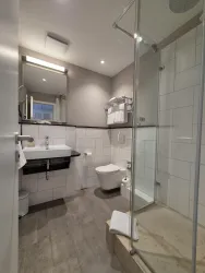 Ein modernes Badezimmer mit einer Dusche und einem Waschbecken. Die Wände sind in hellen Farben gehalten, und es sind Handtücher sichtbar.