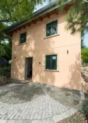 Ein modernes, zweigeschossiges Haus mit einer peachfarbenen Fassade. Der Eingangsbereich hat einen gepflasterten Weg und grüne Fenster.