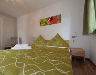 Ein gemütliches Schlafzimmer mit einem großen Bett und grüner Bettwäsche. An der Wand hängt ein Bild mit bunten Blumen.