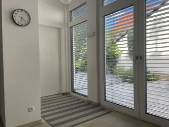 Ein heller Eingangsbereich mit großen Fenstern und Außenjalousien. Im Hof befindet sich ein Parkplatz für Sie.