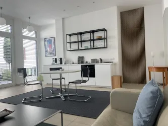 Eine moderne und helle Wohnküche mit einem Essbereich und minimalistischer Einrichtung. Der Raum besticht durch seine Helligkeit und seine stylische Atmosphäre.