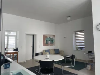 Ein modernes Wohnzimmer mit einem runden Esstisch und modernen Stühlen. Es gibt ein Sofa und einen Designer-Schreibtisch.