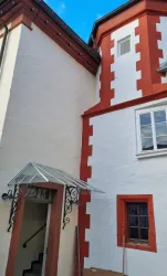 Ein historisches Gebäude mit einer Kombination aus weißen und roten Wänden. Der Eingangsbereich ist mit einem modernen Vordach versehen.