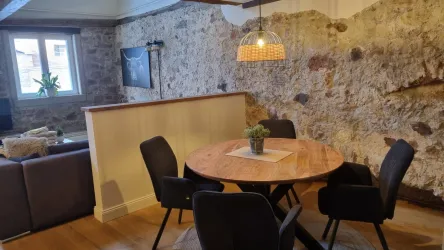 Ein gemütlicher Essbereich mit einem runden Holztisch und schwarzen Stühlen. Die Steinwand und die schöne Beleuchtung schaffen eine warme Atmosphäre.