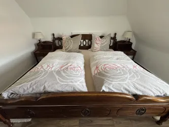 Ein gemütliches Schlafzimmer mit einem großen Doppelbett und zwei Nachttischen. Die Bettwäsche ist mit einem floralen Muster in Rosa verziert.