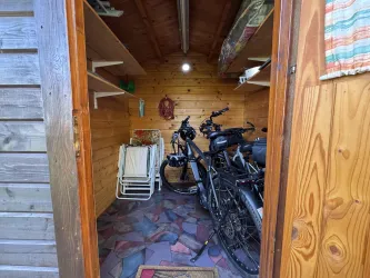Ein kleiner, geräumiger Abstellraum mit Fahrrädern und Regalen. Der Boden ist mit bunten Steinen gestaltet und die Wände sind aus Holz.