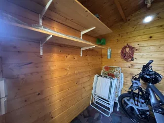 Ein Raum mit Holzvertäfelung, der Regale und einen Fahrradständer zeigt. Auf dem Boden stehen zusammengeklappte Stühle und weitere Gegenstände.