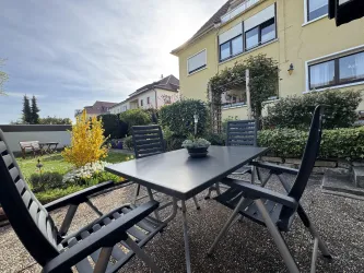 Ein gemütlicher Garten mit einem Tisch und Stühlen. Im Hintergrund sind ein gepflegter Rasen und ein Wohnhaus sichtbar.