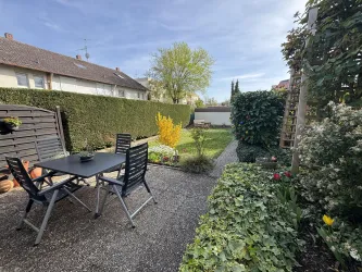 Ein schöner Garten mit einem Tisch und Stühlen zum Entspannen. Grüne Pflanzen und bunte Blumen schaffen eine einladende Atmosphäre.