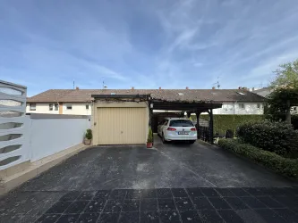 Ein Haus mit einer Garage und einem überdachten Parkplatz. Der Himmel ist klar und es sind einige Pflanzen im Vorgarten zu sehen.
