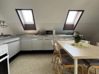 Eine moderne Küchenecke mit einem Tisch und Stühlen. Fenster sorgen für Tageslicht und eine helle Atmosphäre.