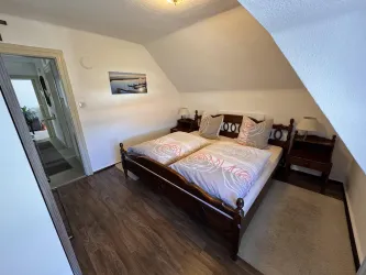 Ein gemütliches Schlafzimmer mit zwei Einzelbetten und modernen Holzmöbeln. An der Wand hängt ein Kunstwerk und es gibt eine Tür zu einem anderen Raum.