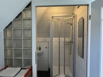 Ein modernes Badezimmer mit einer Duschkabine und Waschbecken. Die Wände sind hell gefliest, und es gibt viel Licht.