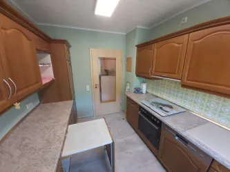 Eine moderne Küche mit Holzmöbeln und hellgrünen Wänden. Der Raum ist gut beleuchtet und umfasst verschiedene Küchengeräte.