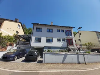 Ein modernes Mehrfamilienhaus mit einer weißen Fassade und roten Akzenten. Vor dem Gebäude stehen mehrere Autos und es gibt eine gepflegte Auffahrt.
