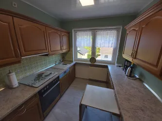 Eine gemütliche Küche mit Holzmöbeln und einem großen Fenster. Der Raum ist hell und gut ausgestattet mit modernen Geräten.