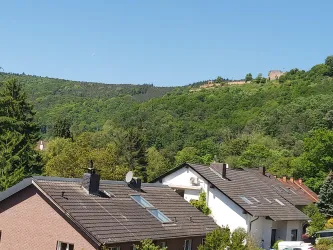 Eine ruhige Wohngegend mit modernen Häusern. Im Hintergrund sind grüne Hügel und ein Teil einer Burgruine zu sehen.