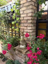 Eine charmante Gartenmauer aus Ziegelsteinen mit bunten Blumen. Eine dekorative Statue steht zwischen den leuchtend roten Rosen.