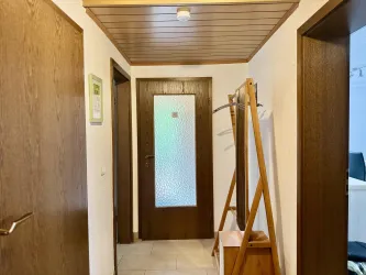 Ein heller Flur mit Holzverkleidung und mehreren Türen. An der Wand steht ein Garderobenständer.
