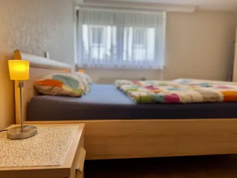 Ein gemütliches Schlafzimmer mit einem Bett und bunten Bettdecken. Neben dem Bett steht ein Nachttisch mit einer Lampe.