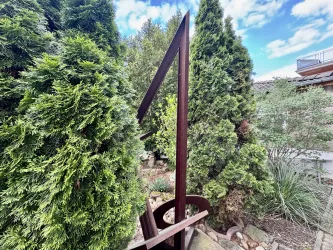 Eine moderne Skulptur in Form der Zahl vier, umgeben von grünen Büschen. Der Himmel ist klar und blau, was eine ruhige Atmosphäre schafft.