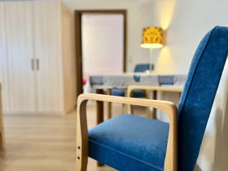 Ein moderner Raum mit einem blauen Stuhl und einem Tisch im Hintergrund. An der Wand befindet sich ein Schrank und eine dekorative Lampe.
