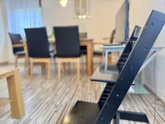 Ein modernes Esszimmer mit einem Tisch und schwarzen Stühlen. Der Boden hat ein Holzdesign und das Licht ist hell und einladend.