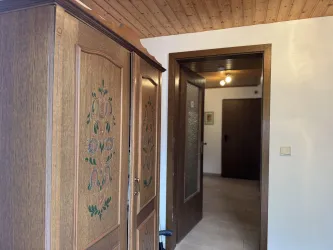 Ein Flur mit einem Holzschrank und einer offenen Tür zu einem anderen Raum. Die Wände sind neutral und die Decke aus Holz.