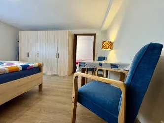Ein geräumiges Schlafzimmer mit einem großen Bett und einem Holzschrank. Ein blauer Stuhl und eine Lampe verleihen dem Raum eine angenehme Atmosphäre.