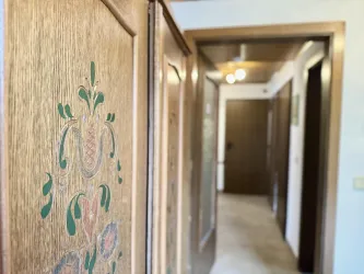 Ein verziertes Holzpaneel in einem Flur. Im Hintergrund sieht man eine helle Tür und eine weitere Wand.
