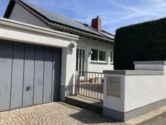 Ein modernes Haus mit hellem Außenputz und einem Garagentor. Der Eingangsbereich ist gepflegt und von einer Hecke umgeben.