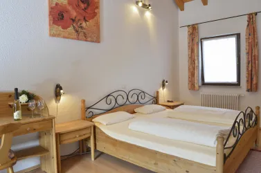 Ein gemütliches Schlafzimmer mit einem Doppelbett aus Holz und einem kleinen Tisch. Die Wände sind hell und das Zimmer hat große Fenster mit Vorhängen.