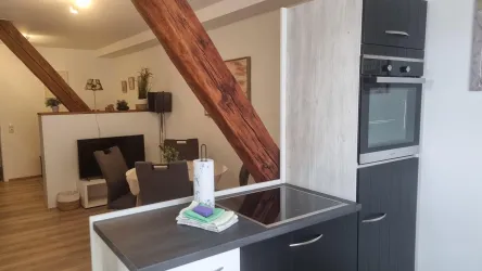 Eine moderne Küche mit Holzdetails und einem eleganten Herd. Im Hintergrund ist ein gemütlicher Wohnbereich sichtbar.