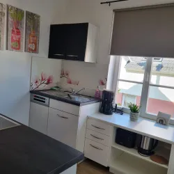 Eine moderne Küche mit weißen und schwarzen Schränken und einer großen Fensterfront. An der Wand sind Blumenmotive und ein kleiner Pflanzentopf auf dem Tisch.